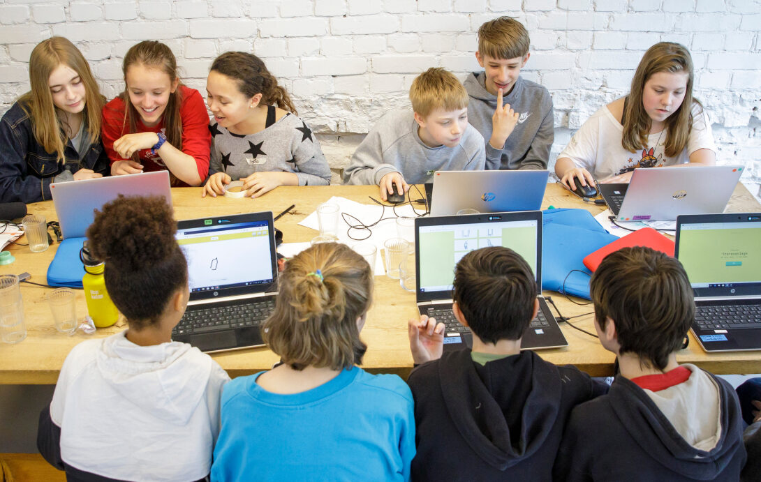 Jugendliche arbeiten an Laptops gemeinsam an einem langen Tisch