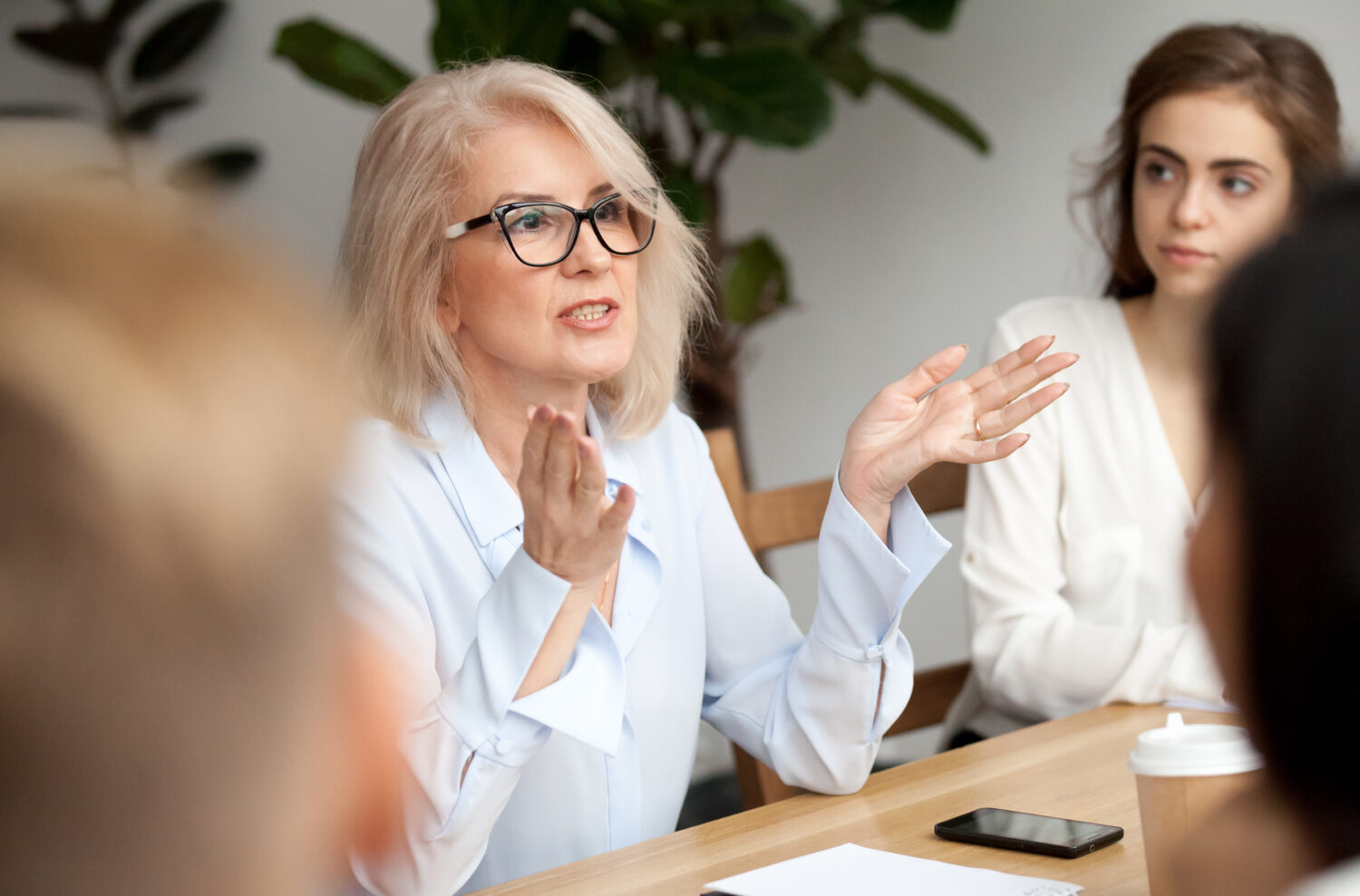 Business-Meeting, Blonde Frau mit Brille gestikulierend im Vordergrund