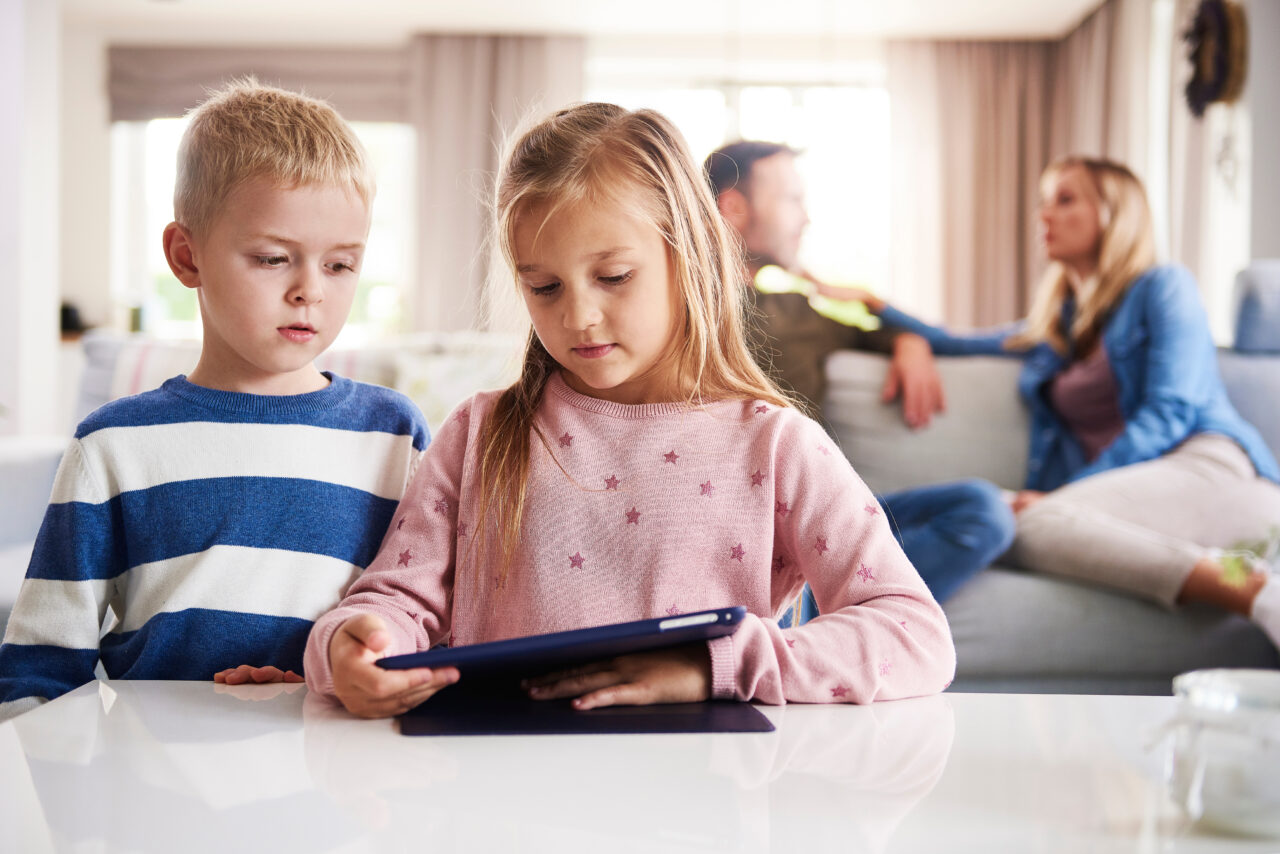 Kinder am Tablet, Eltern verschwommen im Hintergrund zu sehen
